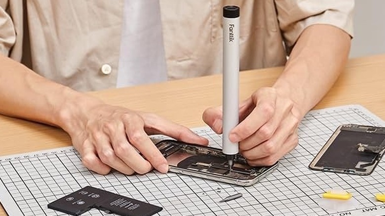 Person using an electric screwdriver to fix a smartphone
