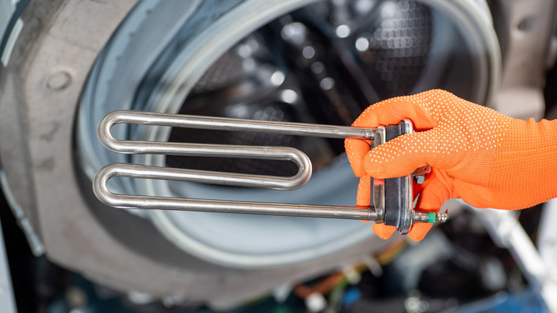 Close up of person holding dishwasher heating element in gloved hand