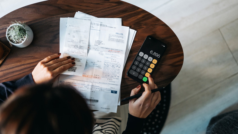 A dark-haired woman works on personal finances at a table.