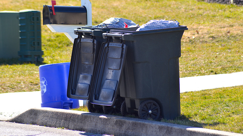 Two black opened trash cans on the curb.