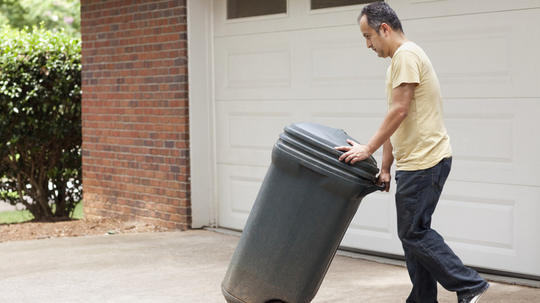 A man wheeling out a trash can outside.