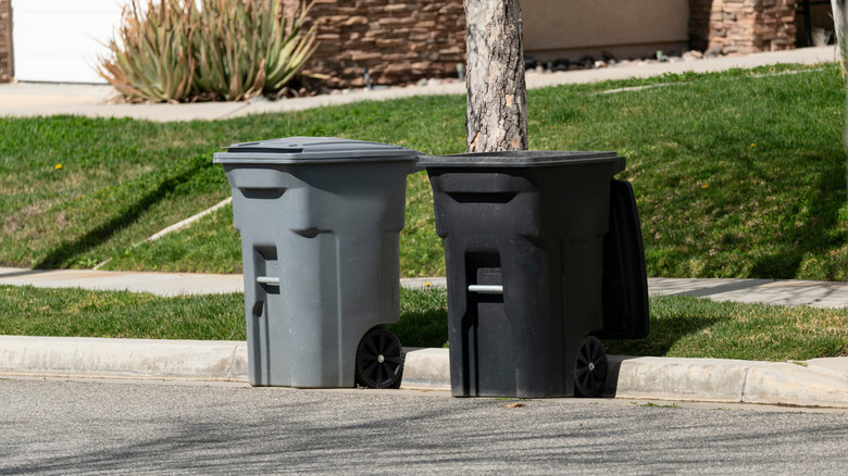 A gray and black trash can on the street.