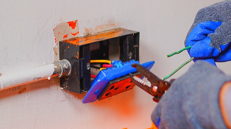 A hand working with orange electrical wiring inside of a wall