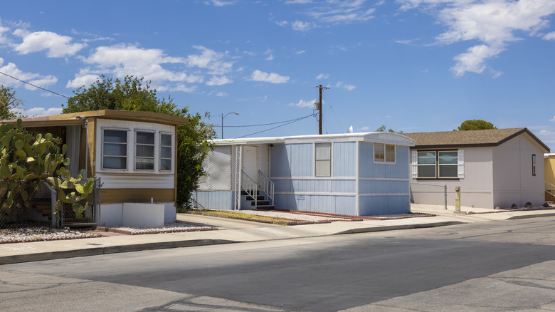 Three mobile homes on a street under sunny skies with small clouds.