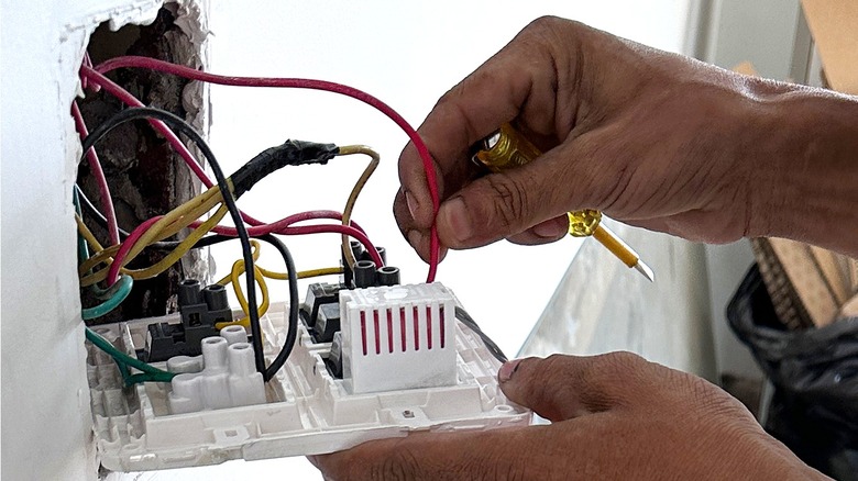 Close-up of a person's hands holding a screwdriver and the red wire of an outlet's wiring bundle