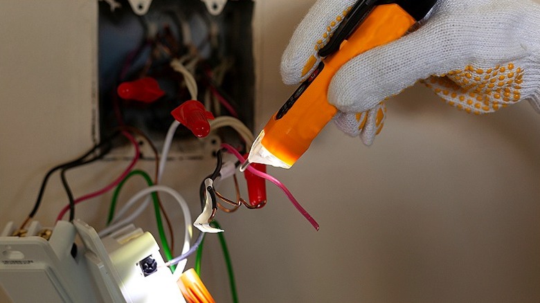 A person's gloved hand uses a voltage tester to test wiring from a wall panel