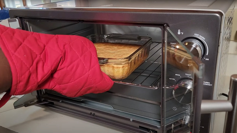 A hand with an oven mitt removes cornbread from the oven