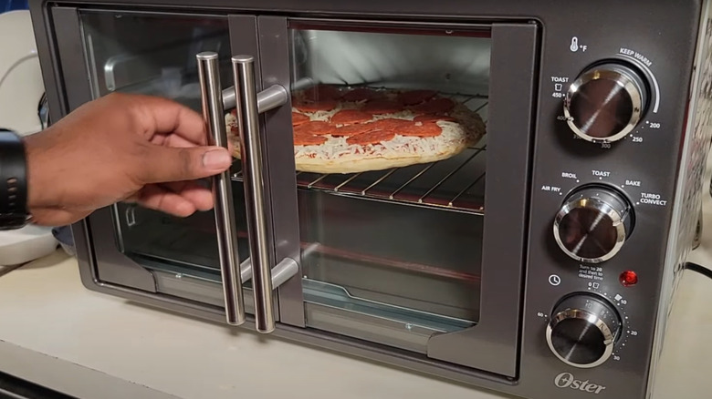 A man putting a frozen pizza in the oven