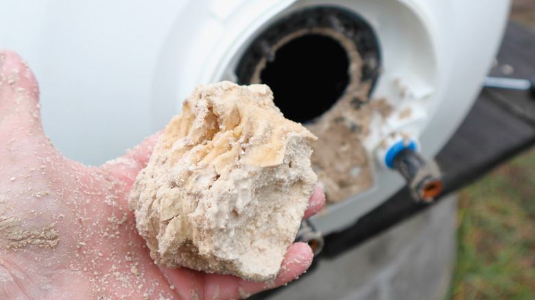 Hand holding calcium deposits from inside of a water heater