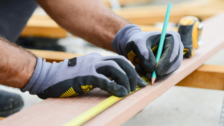 A hand marking a plank of wood using tape measure