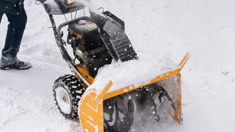 Person using an orange snow blower to clear snow