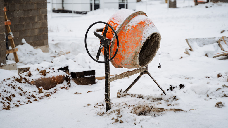 Orange concrete mixer covered in snow behind a building
