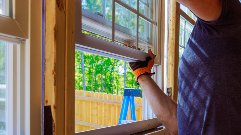 A man in a blue t-shirt installs a new window