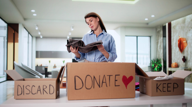 A woman decluttering, with boxes for items she wants to keep, donate, and discard