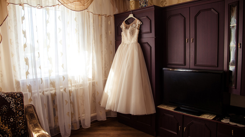 A white wedding dress hanging next to a wooden closet