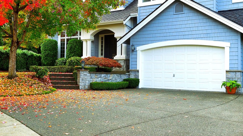 Driveway of a blue house with fallen autumn leaves seen to the left of it