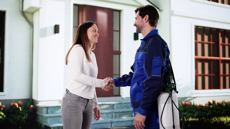 A woman shaking hands with a man in an exterminator outfit outside of a house