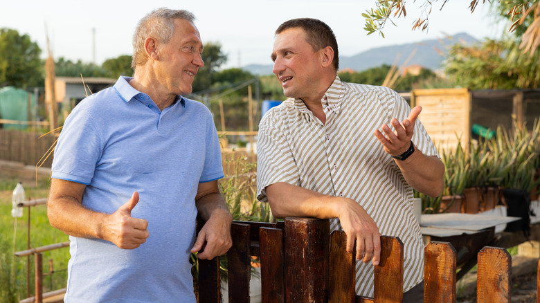 Two neighbors talking near a wood fence