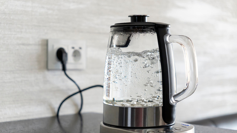 Transparent electric kettle with boiling water on table in the kitchen