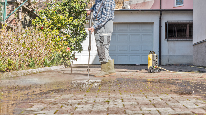 man spraying driveway with water