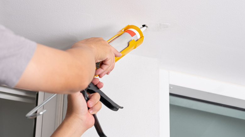 Person using a caulk gun to seal a hole in a home's ceiling