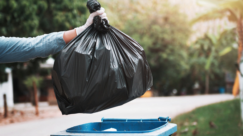 Person placing tied trash bag into trash bin.