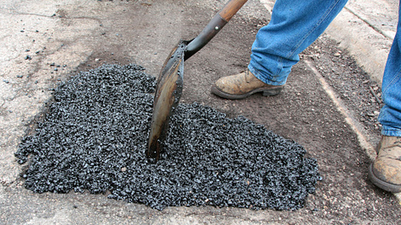 A person wearing work boots and holding a shovel adds an aggregate mixture on top of a sinkhole.