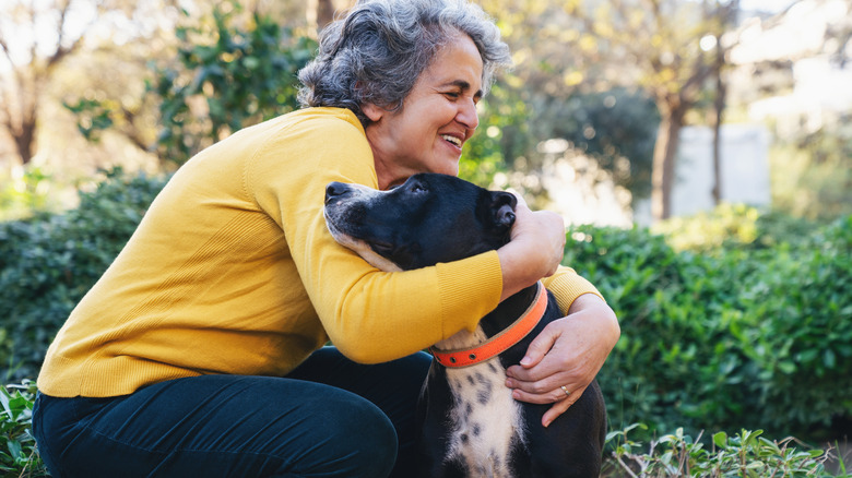 An older woman embracing a black dog