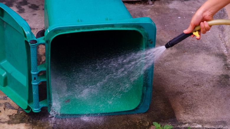Person washing a trash can with a hose
