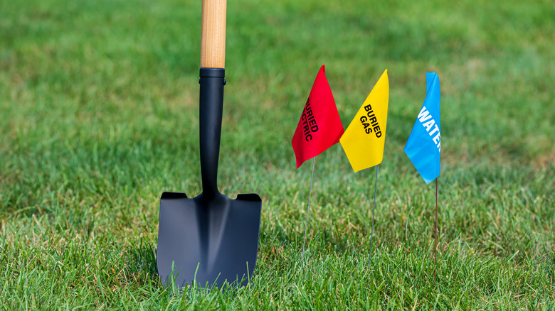 A shovel near red, yellow, and blue utility marking flags.