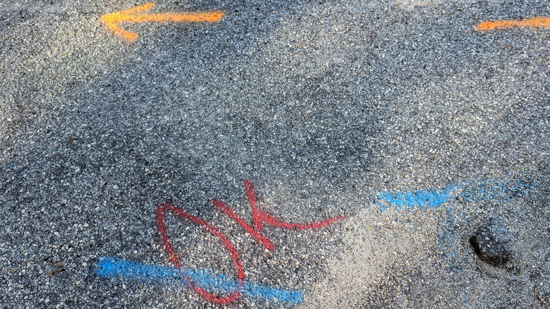 Utility markings on a concrete pavement in red, yellow, and blue.