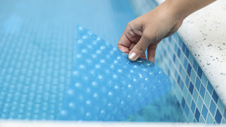 Person putting a solar cover on a pool