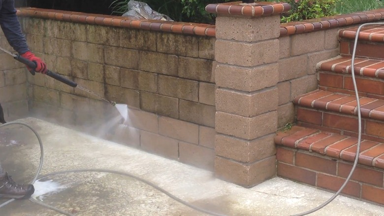 Man pressure washing cinder block retaining wall