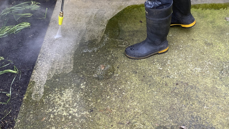 Person pressure washing a dirty concrete driveway