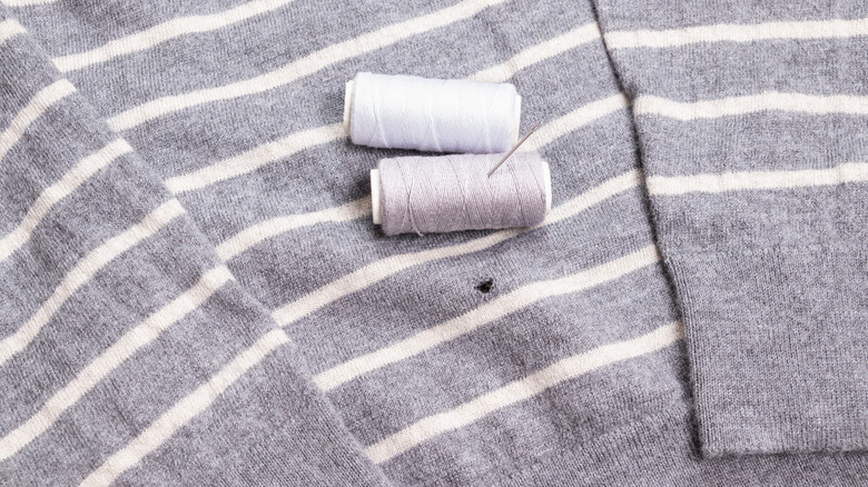 two spools of thread and a needle on a sweater that has a moth hole