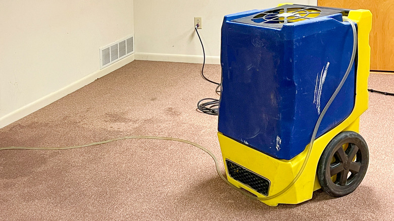 A large portable dehumidifier in a bedroom with damp carpet.