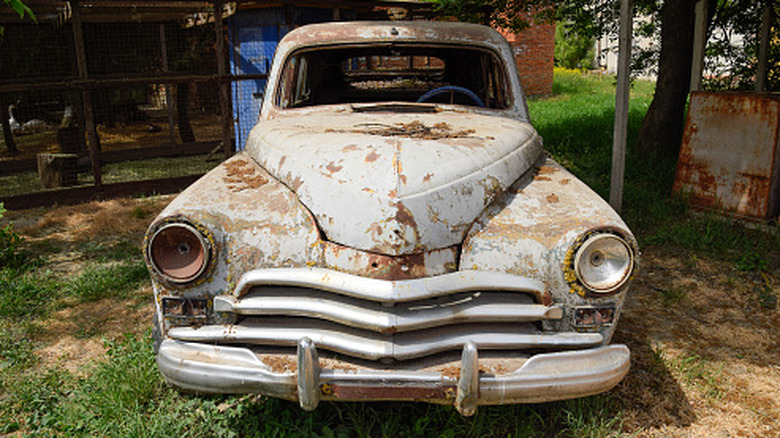 a rusty old car in a yard reduced to scrap metal