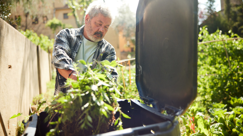 A man throwing weeds int a compost container with a lid