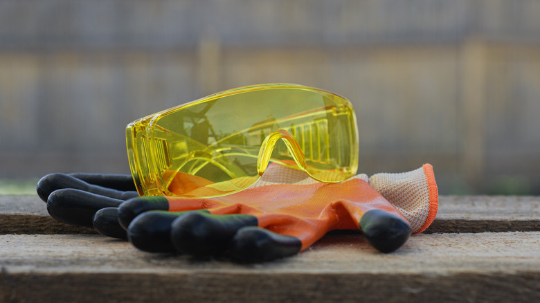 Yellow safety goggles and orange gloves rest on a rustic wooden surface
