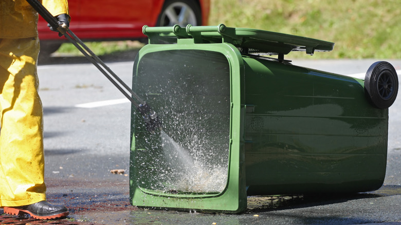 Person in rubber boots spraying out green compost bin