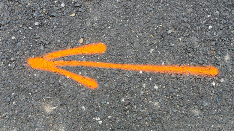 An orange utility marking on an asphalt driveway