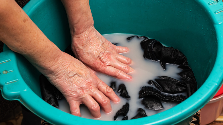 Hands soaking laundry in blue bin