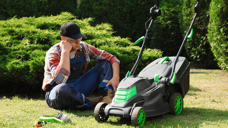 Man sitting beside his broken lawn mower.