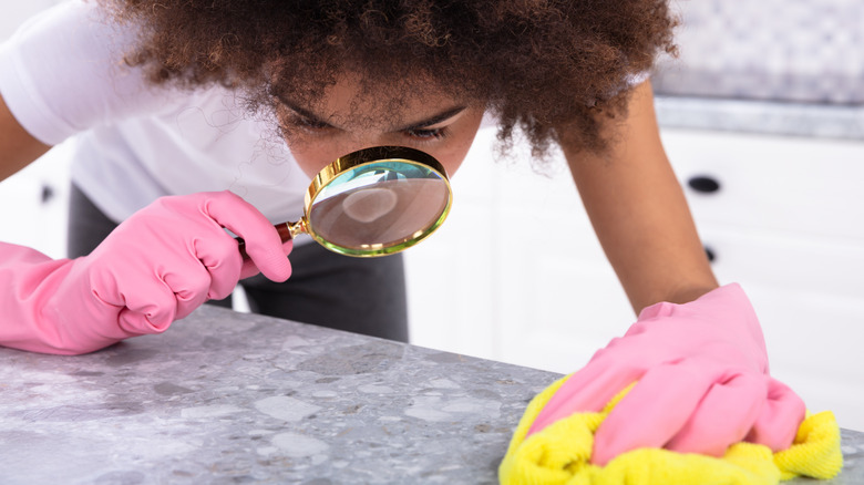 Woman using a magnifying glass to look closely at the kitchen counter while cleaning.