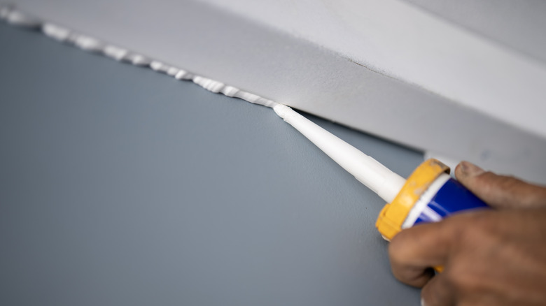Close-up of a male hand caulking the gaps in a ceiling.