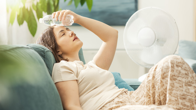 A woman sitting next to a fan with a water bottle on her head in hot weather