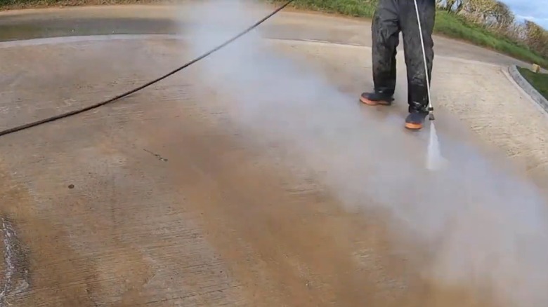 Person pressure washing tire marks off a concrete driveway