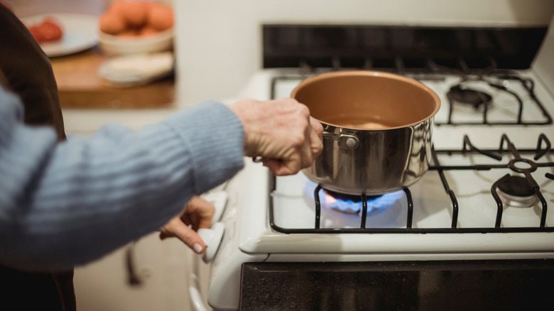 A person putting a saucepan of water on a gas stove.