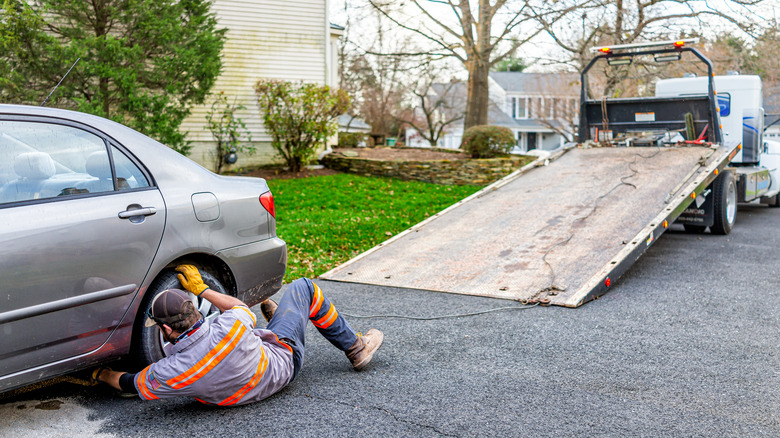 A man prepares to tow a gray car out of a driveway