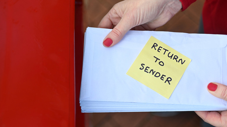 Closeup of hands putting letters in a red mailbox with 'return to sender' note